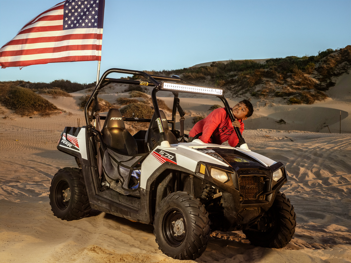 Boy in ATV on beach with large American Flag